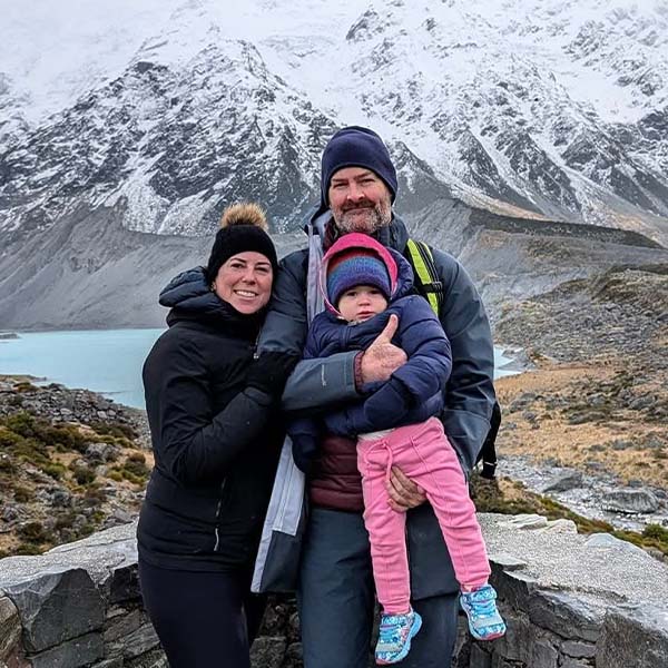 Happy family in front of a large glacier and bay wearing hats and large coats.