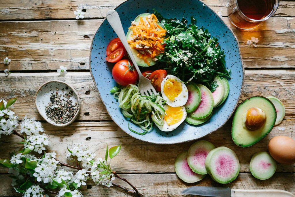 Large, healthy salad with fresh vegetables and eggs on a wooden table. Healthy nutrition is key during menopause.